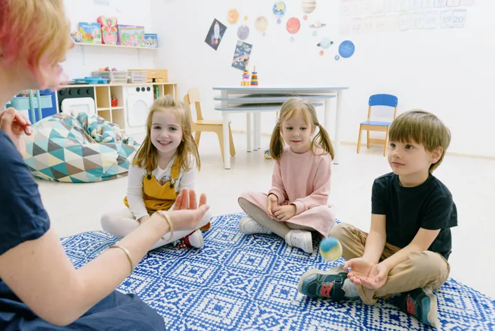 Éducatrice assise avec de jeunes enfants sur un tapis