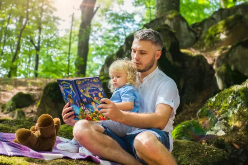 un papa et sa petite fille assise sur ses genoux lisent un livres pour enfant.