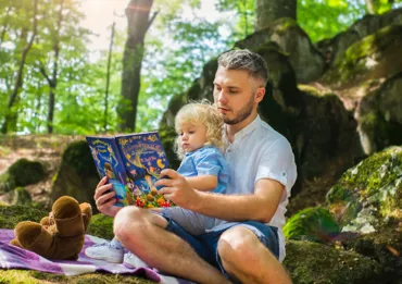un papa et sa petite fille assise sur ses genoux lisent un livres pour enfant.