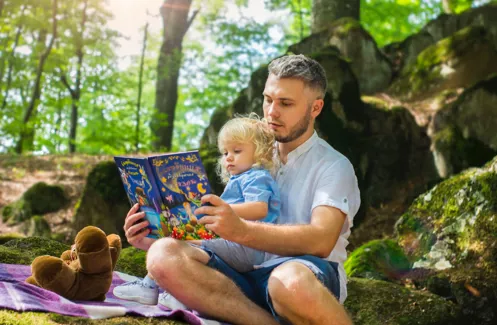 un papa et sa petite fille assise sur ses genoux lisent un livres pour enfant.